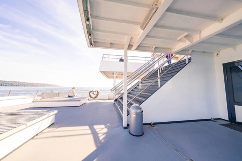 An upper deck of a modern ship with seats and a view of the sea under a blue sky, Schiff Fahrt,