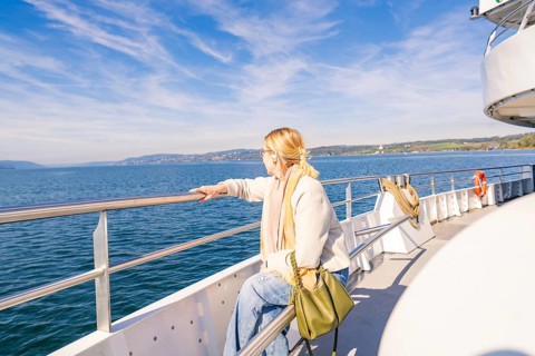 A woman stands relaxed at the railing of a ship and looks out to sea in sunny weather, Schiff