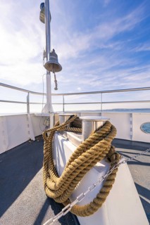 A ship deck with thick ropes and a bell, in front of a clear blue sky at sea, boat trip, Lake