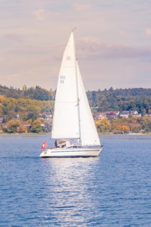 A sailboat sails peacefully on a quiet lake with autumnal landscape in the background, boat trip,