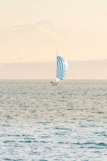Sailing boat with blue and white sail floating on a wide lake against a mountain backdrop, Schiff