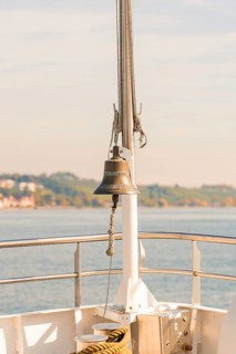 Bell on a ship deck with a view of a sunny coastal landscape, boat trip, Lake Constance, Germany