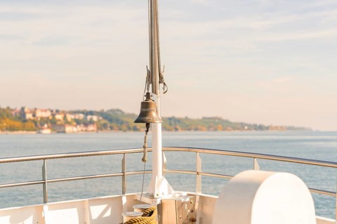View of the water from a ship with a railing and a bell in the foreground, Schiff Fahrt, Lake