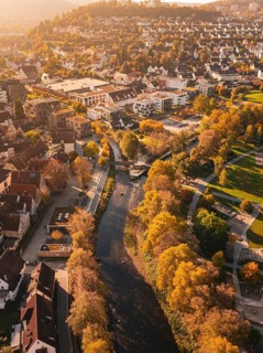 A river flows through an autumnal urban landscape, surrounded by parks and colorful trees, Nagold,