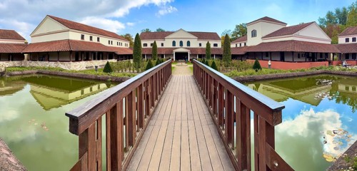 View from site of archaeological open-air museum across small wooden bridge across ornamental pond
