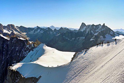 Mountaineers climb over a snow-covered ridge, behind Grandes Jorasses, Aiguille du Midi mountain