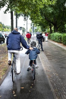 DEU Germany Germany Berlin Cyclists have their arms on a child's back as they cycle towards the