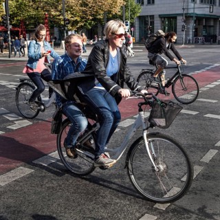 DEU Germany Germany Berlin cyclist transports a man on the luggage rack while another woman watches
