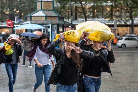 DEU Germany Germany Berlin Young woman walk through the rain, their shopping bags as protection