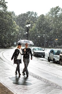 DEU Germany Germany Berlin A couple walking with an umbrella through a summer rain shower at the