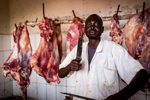 RWA RWANDA Rwanda Kayonza A butcher sharpens his knives in front of pieces of meat. He poses for