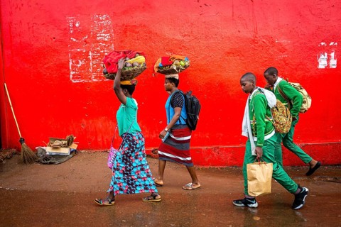 RWA RWANDA RUANDA Kigali People in colourful clothes walk along a red wall