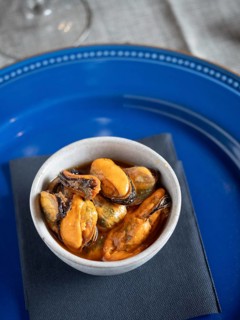 Marinated mussels served as a savory tapa on a rustic white bowl with a blue plate