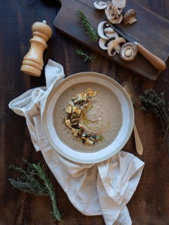 Mushroom soup with rosemary, thyme, garlic croutons, and raw mushrooms on a dark wood background