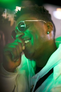 Greenlit African man wearing sunglasses at night as shade of anonymity, laughing, happy, giggle,