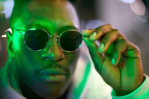 Greenlit African man wearing sunglasses at night as shade of anonymity, coolness, approved