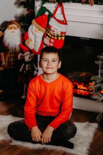 Boy sitting on a white rug in front of a fireplace with christmas decorations.Belarus