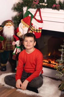 Young boy smiling, sitting on a rug with christmas decorations and a lit fireplace.Belarus