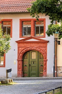Historic building façade with green door and decorative red stone decorations, surrounded by trees