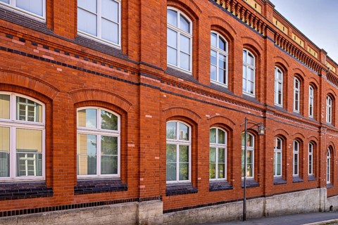 Classic red brick façade of a building with white windows under a blue sky, brick façade of