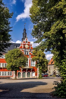 Historic building with tower and red accents, surrounded by trees, The old town of Arnstadt in