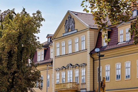 Historic baroque building with yellow façade, decorated gable, surrounded by trees, the façade of