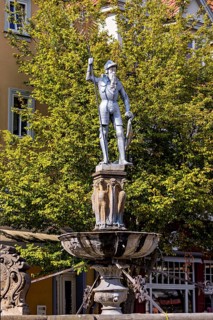 Metal statue of a warrior on a fountain surrounded by green trees, statue and monument in the old