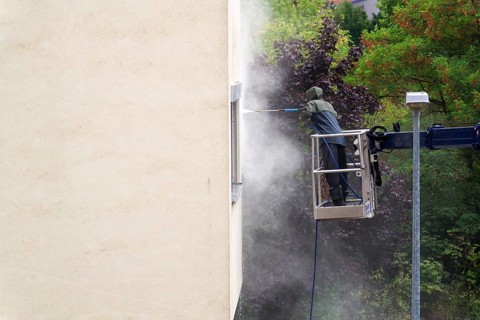 Unrecognizable man cleaning facade surface from lifting platform with high pressure stream of water