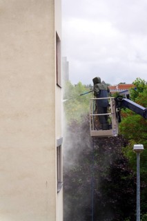 Unrecognizable man cleaning facade surface from lifting platform with high pressure stream of water