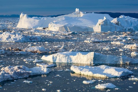 A massive iceberg and iceberg fragments rising from a frozen sea, Ilulissat Icefjord, Greenland