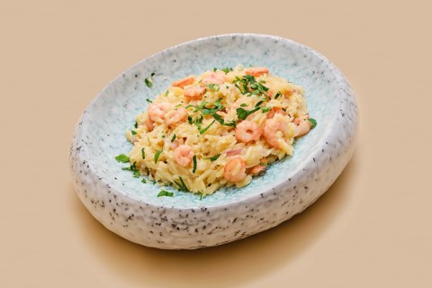 Risoni pasta mixed with tender shrimp is presented on a stylish plate. The dish is topped with