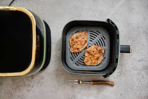 Two cooked seasoned pork sirloin cutlets in the basket of an air fryer. The kitchen setting