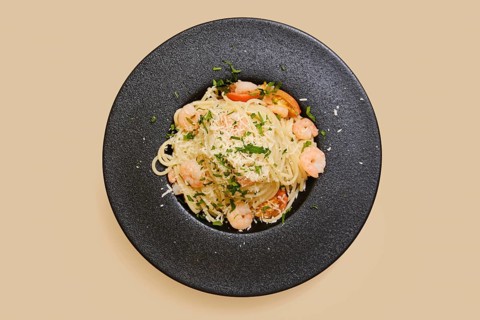 Delicious creamy garlic shrimp pasta in a black plate, garnished with herbs and cheese. This