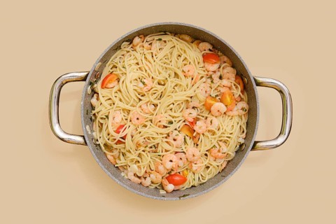 Overhead view of creamy garlic shrimp pasta in a large pan. Plump shrimp and colorful tomatoes