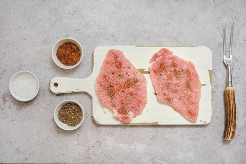 Two pork sirloin chops on a cutting board, seasoned with various spices, in a well-lit kitchen.