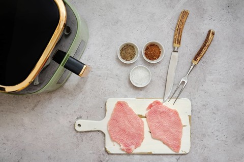 Two raw pork sirloin cutlets are placed on a cutting board next to small bowls filled with spices.