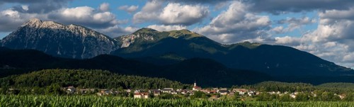 A Slovenian village is nestled between green fields and the imposing peaks of the Julian Alps near