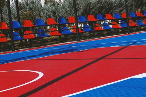 A brightly colored basketball court features bold red and blue sections under the clear sky.
