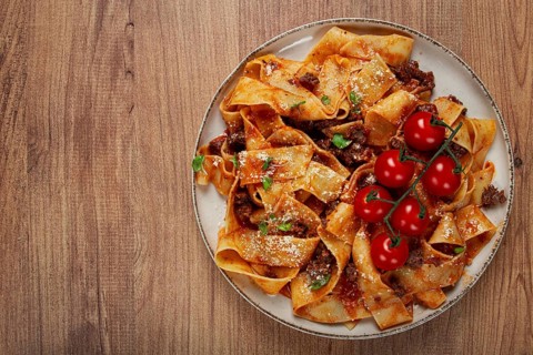 Pappardelle pasta with bolognese sauce, topped with parmesan cheese and cherry branch, homemade, no