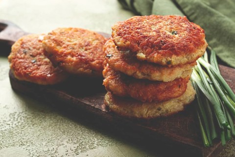 Crispy potato pancakes Latkes, stacked on a wooden board next to fresh green onions, natural light,