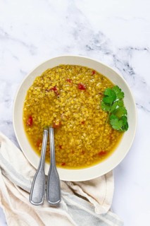 A warm bowl of lentil soup features a golden broth filled with spices and herbs. Fresh cilantro