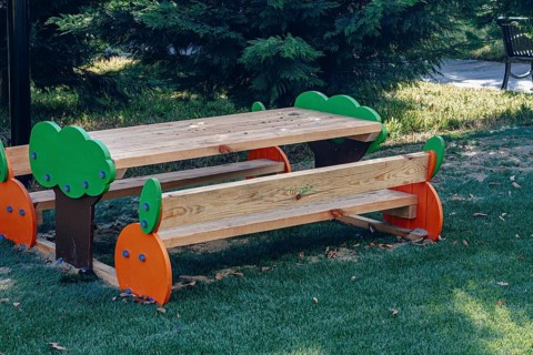 A vibrant wooden picnic table with colorful tree designs stands in a green park, surrounded by