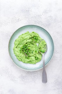 A vibrant green pea puree fills a shallow bowl, topped with fresh peas and microgreens. The dish