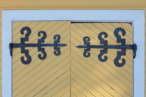 Closeup of old wrought iron decorative hinges on yellow painted wooden doors, Suurikylä, Finland