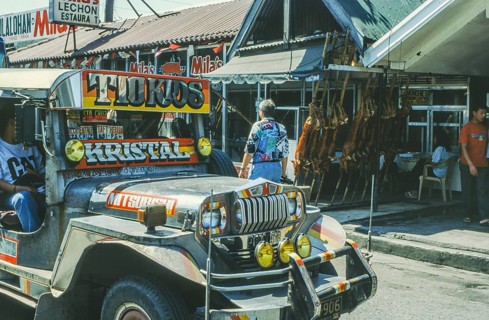 Jeepney minibus in front of a restaurant with skewered suckling pig, Lechon, Manila in 1995,