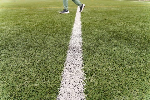 Person walking across a white line on a green artificial turf soccer field, representing progress