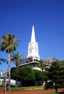 A tall white clock tower surrounded by palm trees, one of the main architectural landmarks for