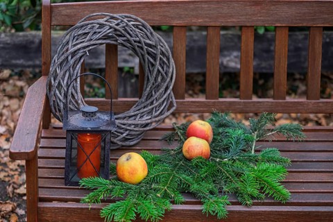 Wooden bench with apples, pine branches, wreath and lantern in rustic style, North