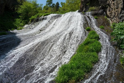 A wide waterfall flows steeply down, flanked by green plants and rocks in nature, Jermuk Waterfall,
