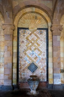 Detailed mosaic with decorative patterns and reliefs on the wall above a stone jug, spring, mineral
